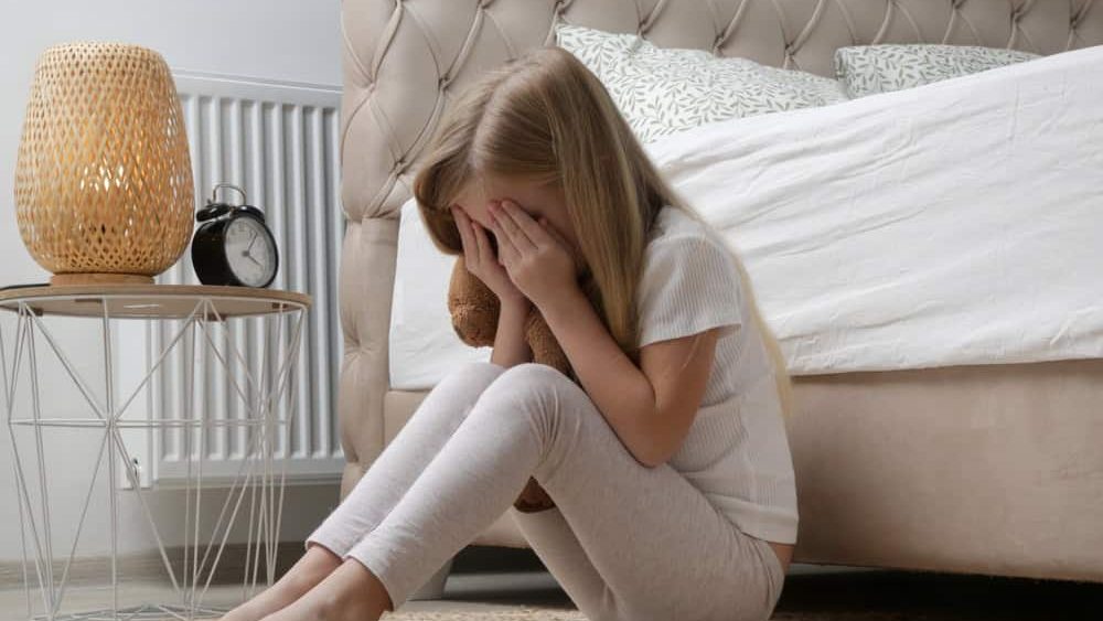 Little girl sitting in the bedroom, crying and covering face with hands