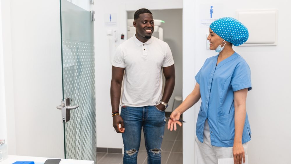 A dental hygienist and an African male patient enter the treatment room for a consultation in a modern clinic. Concept of personalized patient care and professionalism.