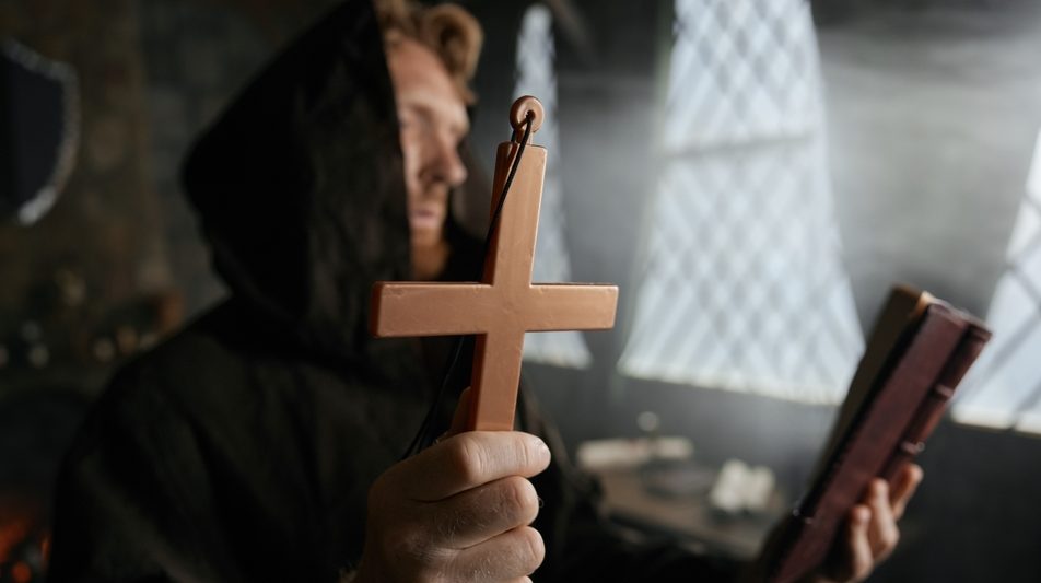 Priest holding cross and holy bible performing exorcism rite