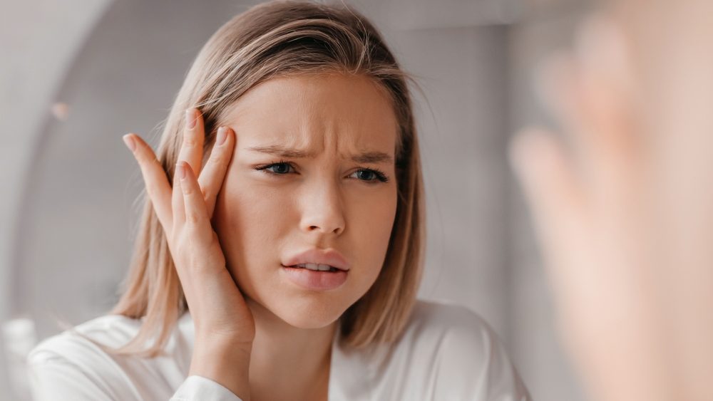 Mirror reflection of upset lady looking at mirror and touching her forehead, having dry skin problem, first wrinkles