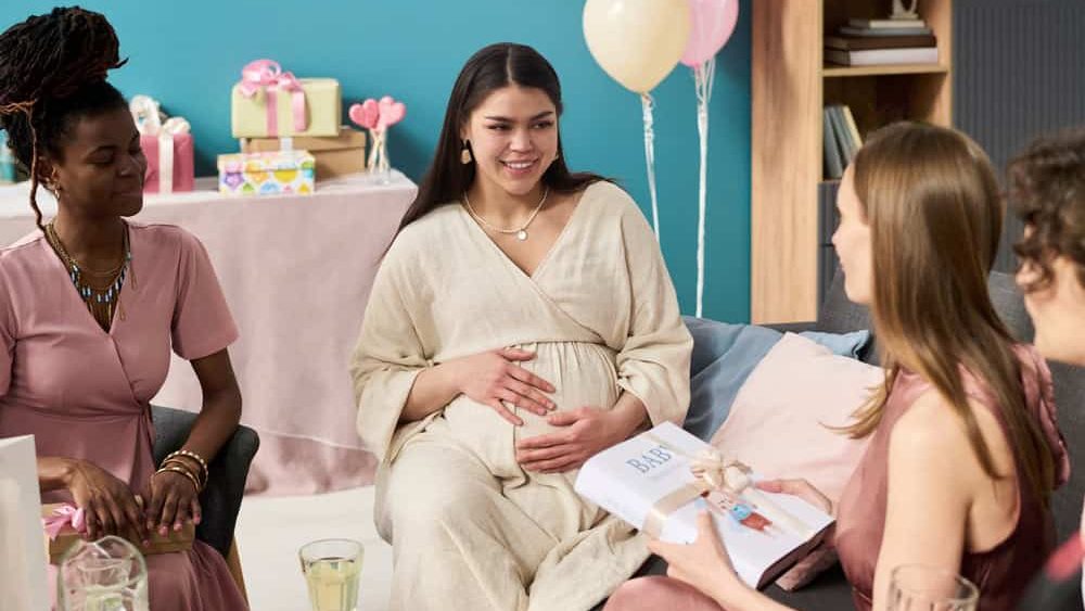 Young pregnant Caucasian woman smiling and holding belly while friends showing baby announcement card at gender reveal party