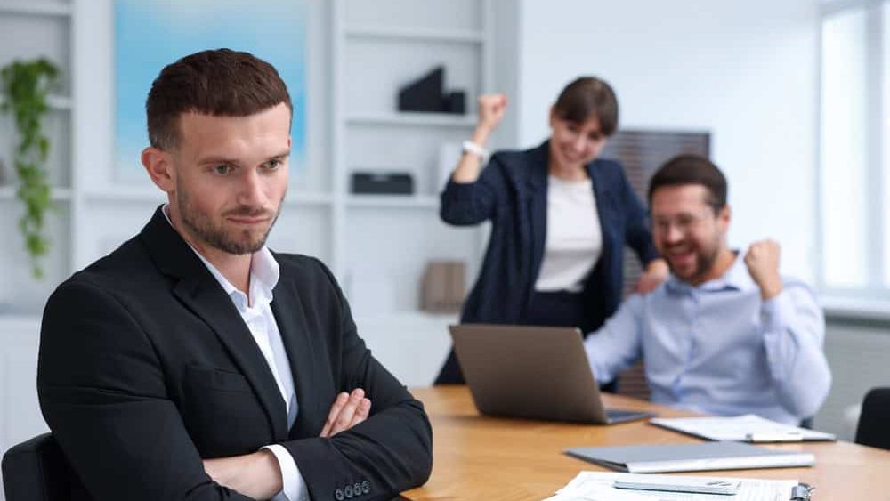 Man feeling jealous of his colleague's success in office, selective focus