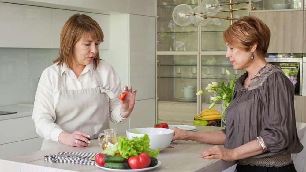 Mature female couple cooking, talking and having fun together on kithen at home. Healthy woman, person indoor lifestyle portrait