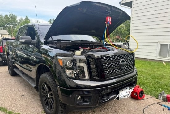Black pickup truck with open hood undergoing on-site repair service.