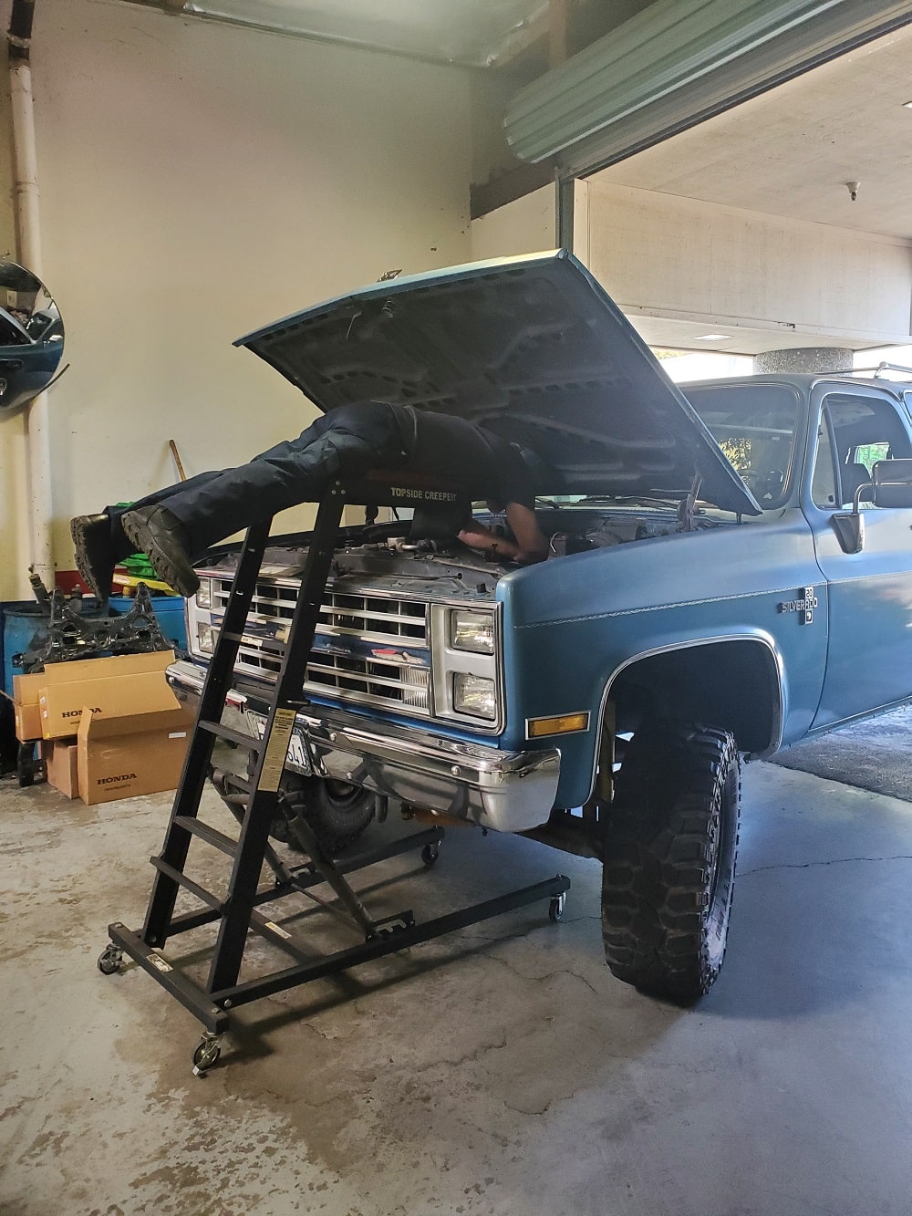 Engine repair with mechanic working under the open hood of a blue truck.