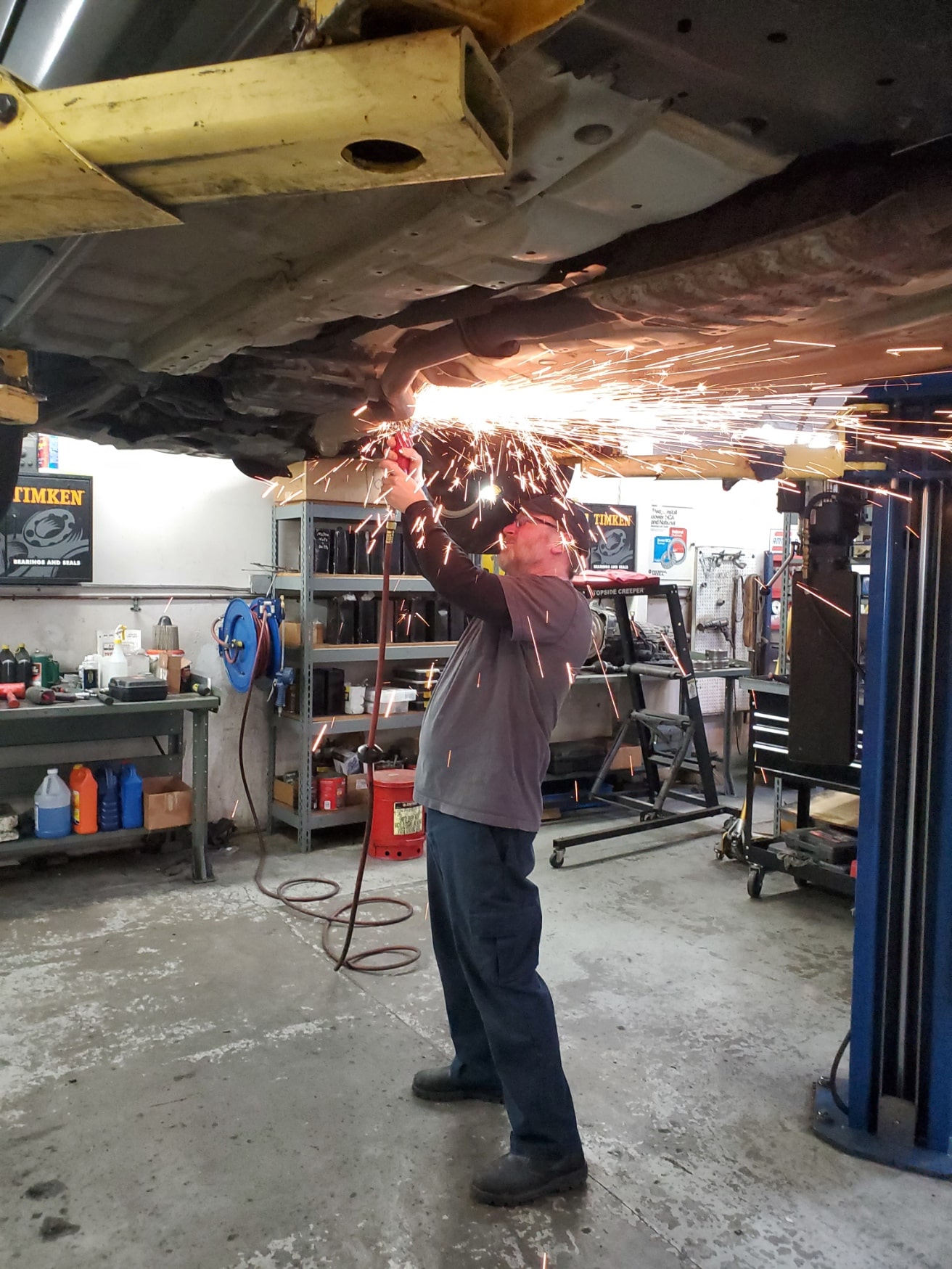 Auto repair technician welding underneath vehicle at Auburn Service Center. Expert car maintenance a.