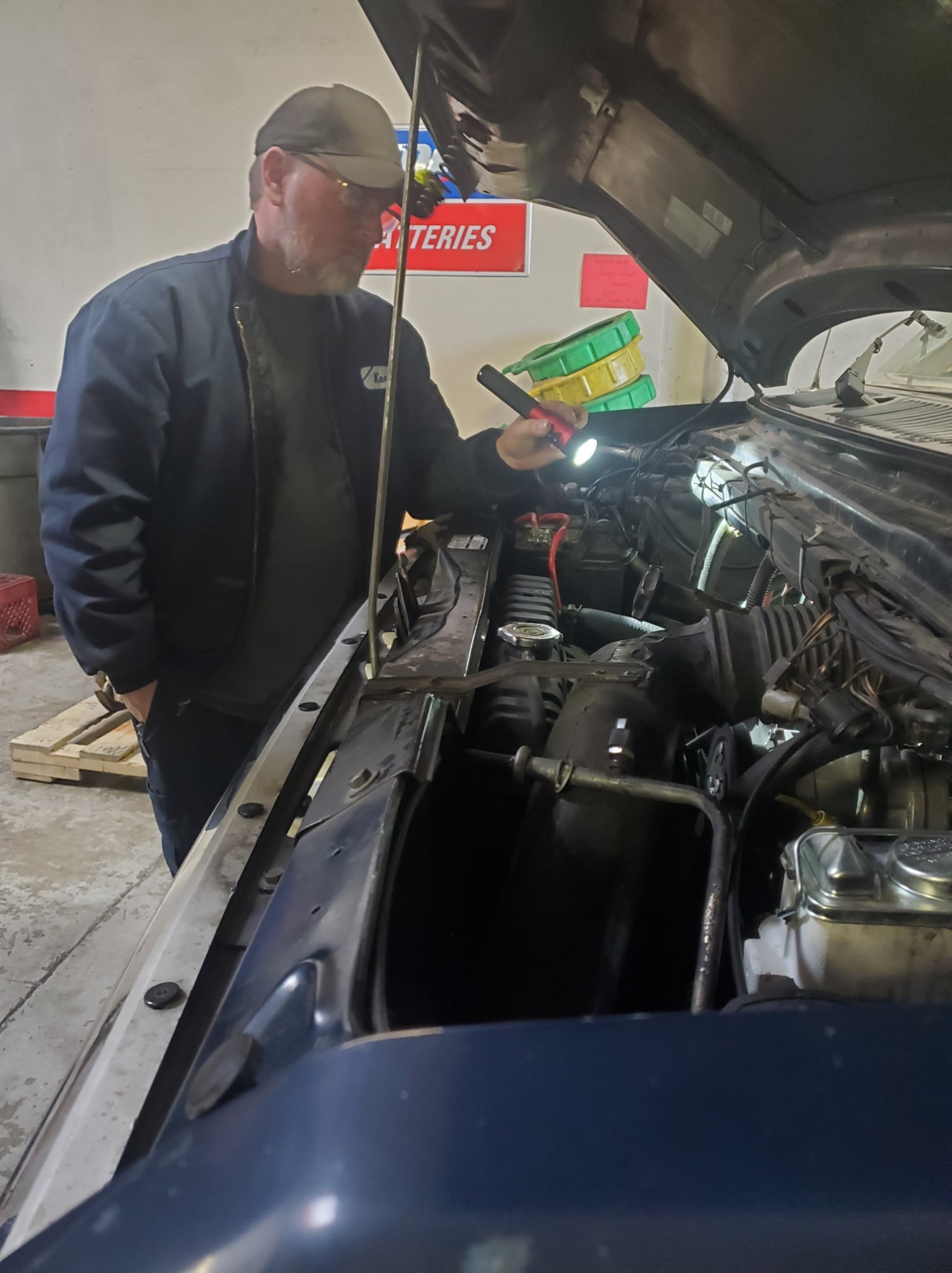 Engine diagnostic technician inspecting vehicle engine with flashlight.