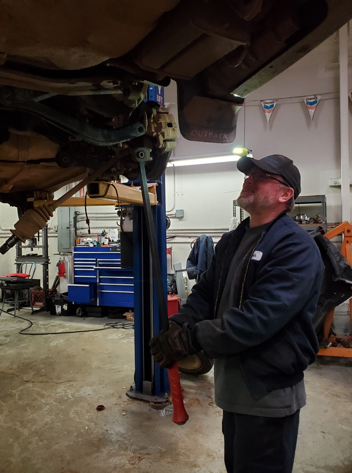 Auto repair technician inspecting vehicle underside in garage.