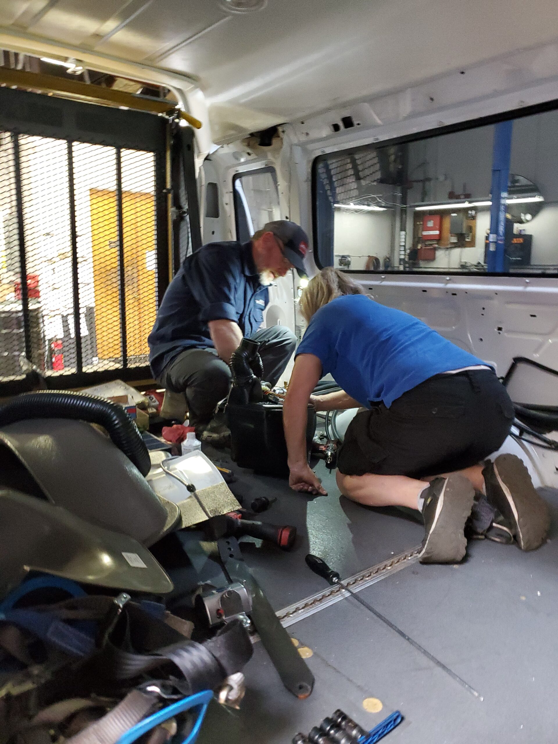 Automotive technicians inspecting and repairing a vehicle inside the service van.