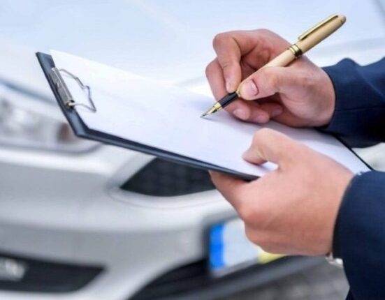 Technician inspecting a car with a clipboard and pen for vehicle service.