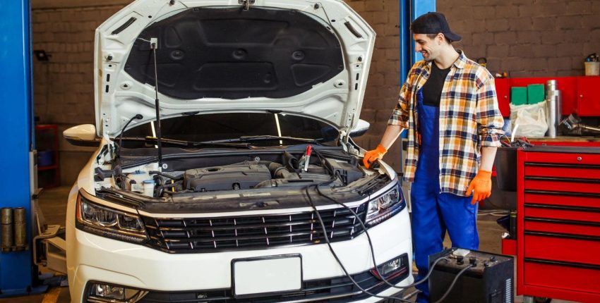 Auto mechanic testing car engine with diagnostic tools at repair shop.