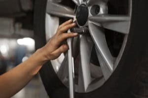Technician adjusting car wheel alignment with a wrench at auto service center.