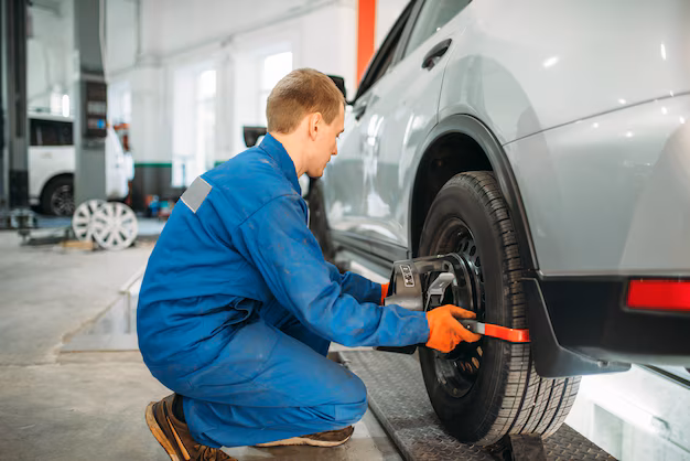 Mechanic adjusting wheel alignment on a car using alignment equipment in a workshop