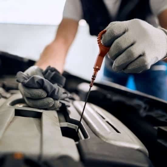 Technician checking engine oil level with dipstick in auto repair service.