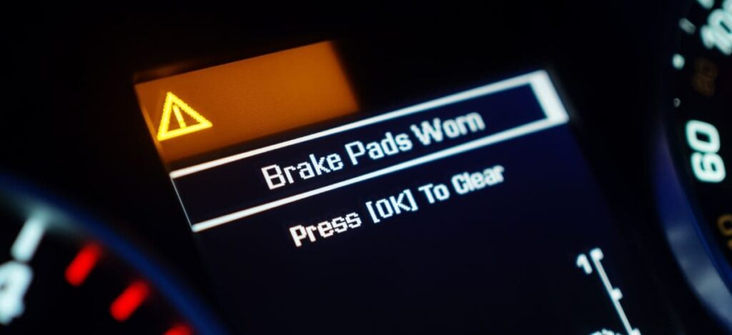 Car dashboard warning light indicating worn brake pads needing attention.