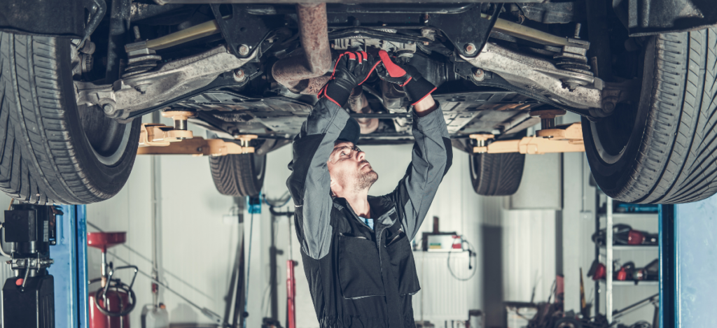 Mechanic inspecting vehicle suspension system in auto repair shop.