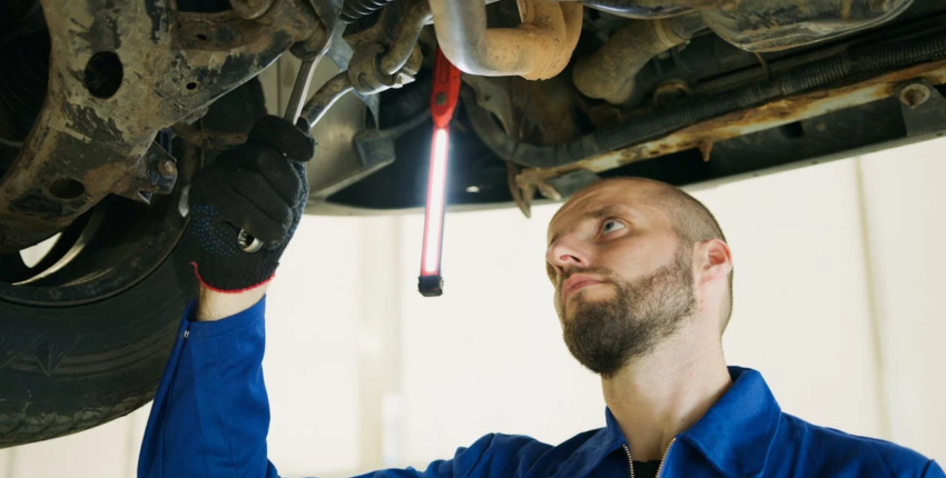 Skilled mechanic inspecting undercarriage of vehicle for repairs.