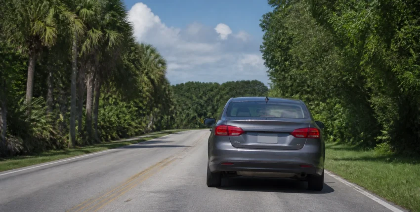 Gray luxury sedan driving on a scenic road surrounded by trees.