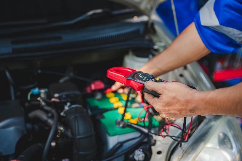 Technician testing car battery with multimeter under the hood.