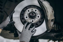 Technician inspecting a car's brake disc and rotor for maintenance.