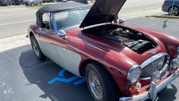 Vintage convertible car with open hood in a parking lot.