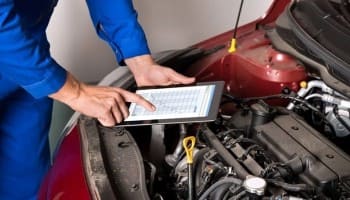 Technician using a tablet for car engine diagnostics under the hood at BC Automotive.