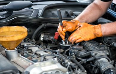 Engine repair technician working on a vehicle engine with tools and gloves.