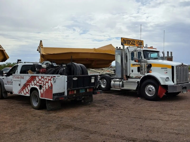Large tow truck with oversize load sign on a dirt lot.