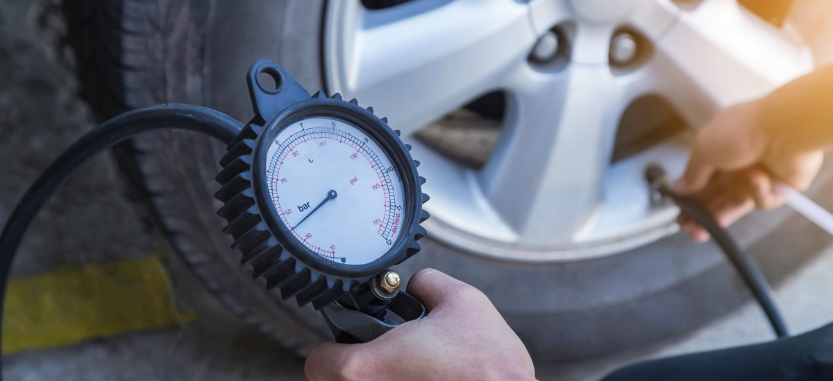 Person measuring tire pressure with a gauge on a car tire outdoors.