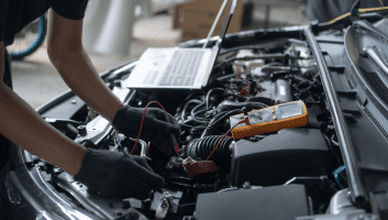 Technician performing engine diagnostics with tools under the hood of a car.