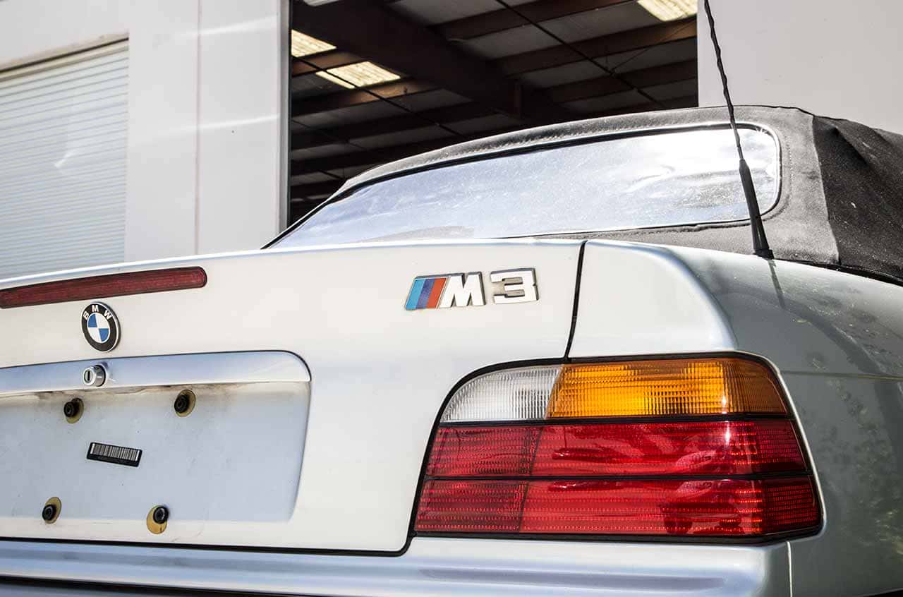 BMW M3 rear with classic design and taillights, parked inside an auto service shop.