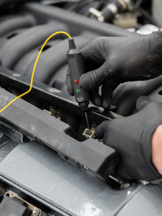 Technician testing car electrical system with diagnostic tool.
