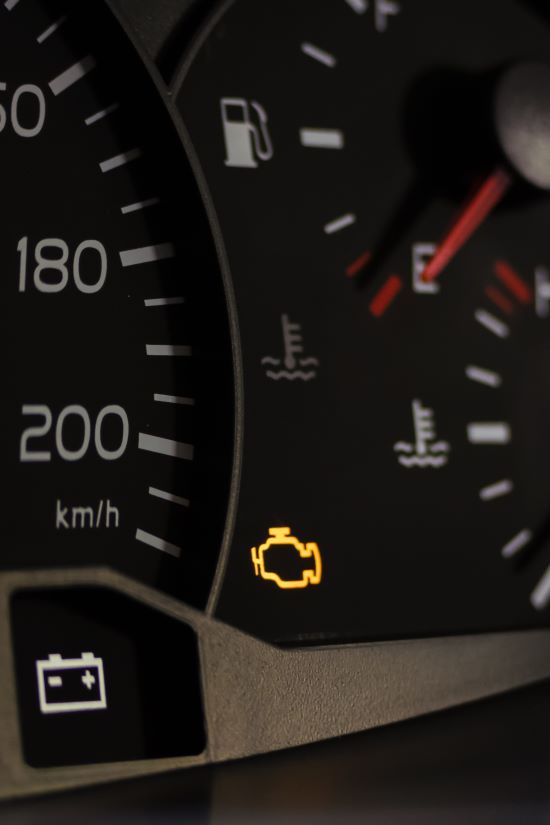 Car dashboard with illuminated check engine light indicator.