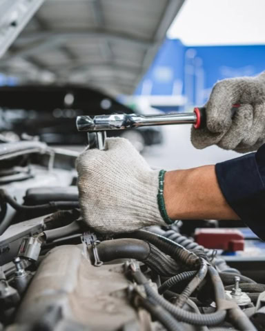 Technician repairing engine with screwdriver in auto repair shop.