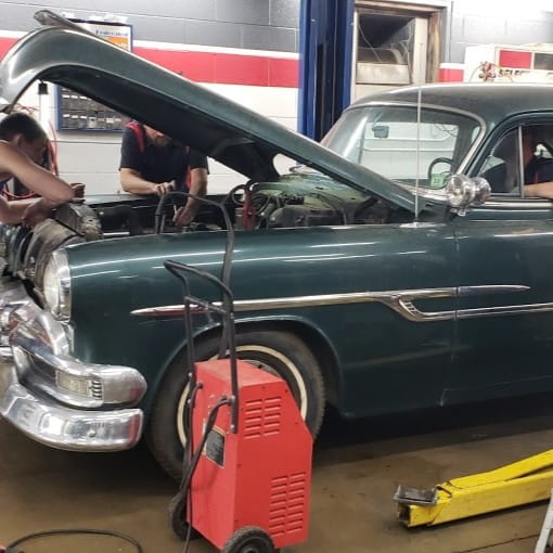Vintage car being repaired in Boise Muffler auto shop with open hood and mechanic work.
