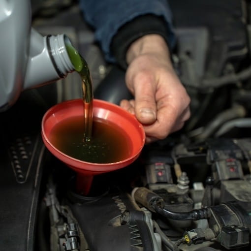 Engine oil being drained into a red container during vehicle maintenance.