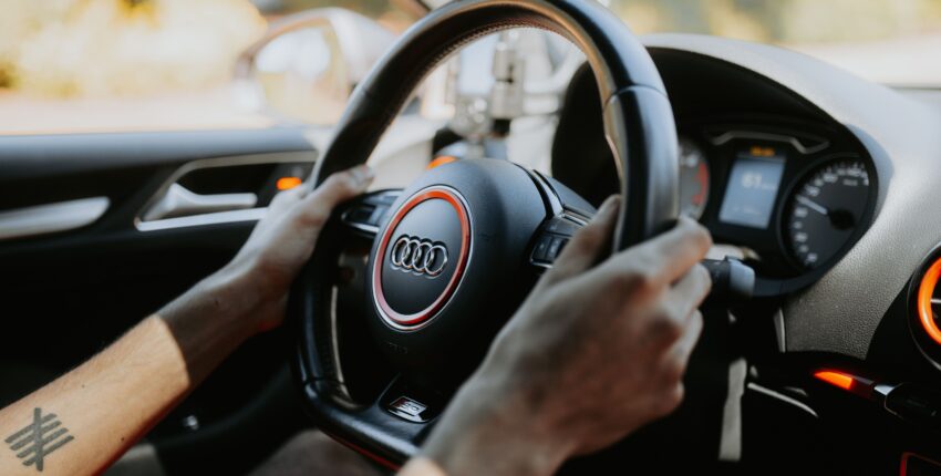 Close-up of a person driving an Audi with focus on the steering wheel.
