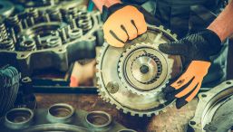 Close-up of a person holding a gear in a workshop setting.