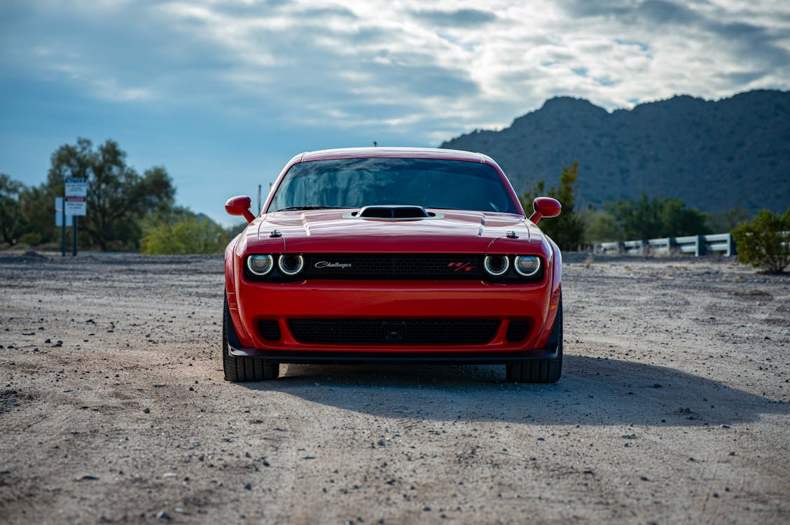 Red Dodge Challenger sports car parked outdoors with mountains in the background.