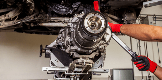 Technician working on a car engine with tools in a repair shop.