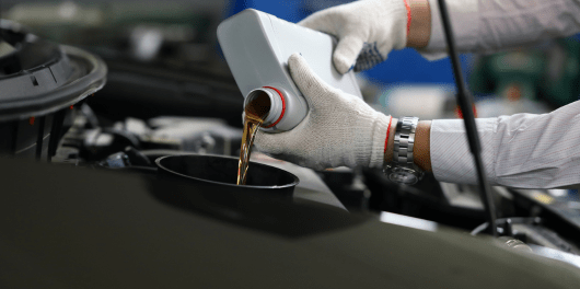 Technician pouring oil into a car engine during an oil change service.