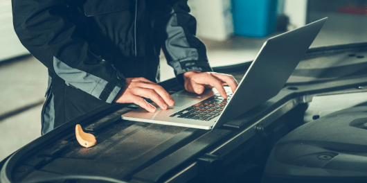 Technician working on car engine with laptop at C&D Automotive.
