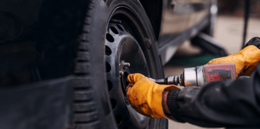 Technician repairing a car tire with a pneumatic wrench at C&D Automotive.
