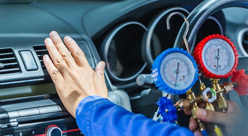 Technician checking car's air conditioning system with gauges.
