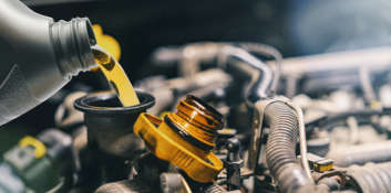 Oil change being performed on a vehicle engine, with fresh oil pouring into the engine bay.