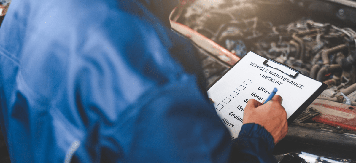Technician reviewing vehicle maintenance checklist under the hood.