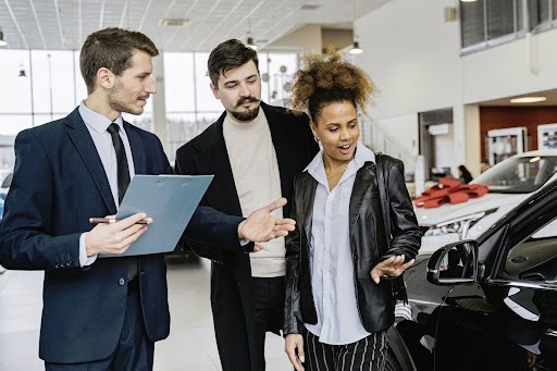 Car dealership staff inspecting a vehicle with a customer.