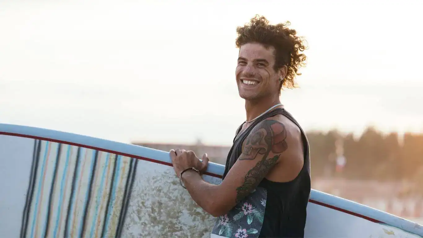 surfer wearing a tanktop and holding a surfboard 