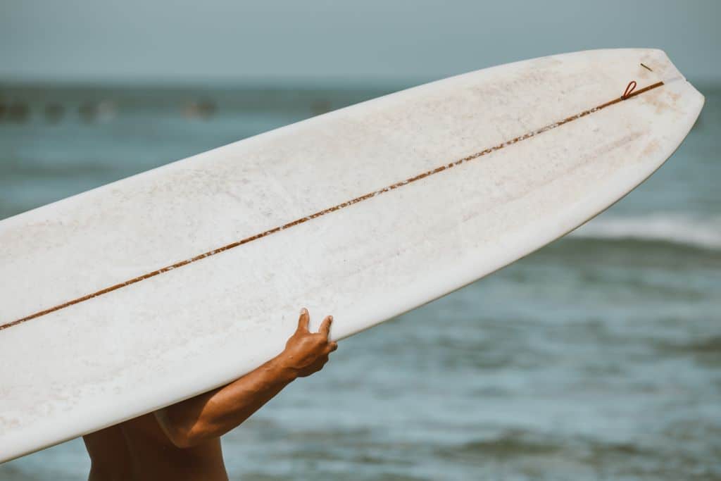 Close-up of a surfer carrying a surfboard on a beach in Hawaii.