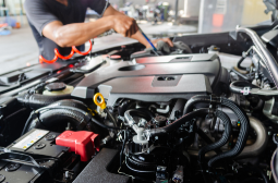 Technician performing oil and filter change in a car engine bay.